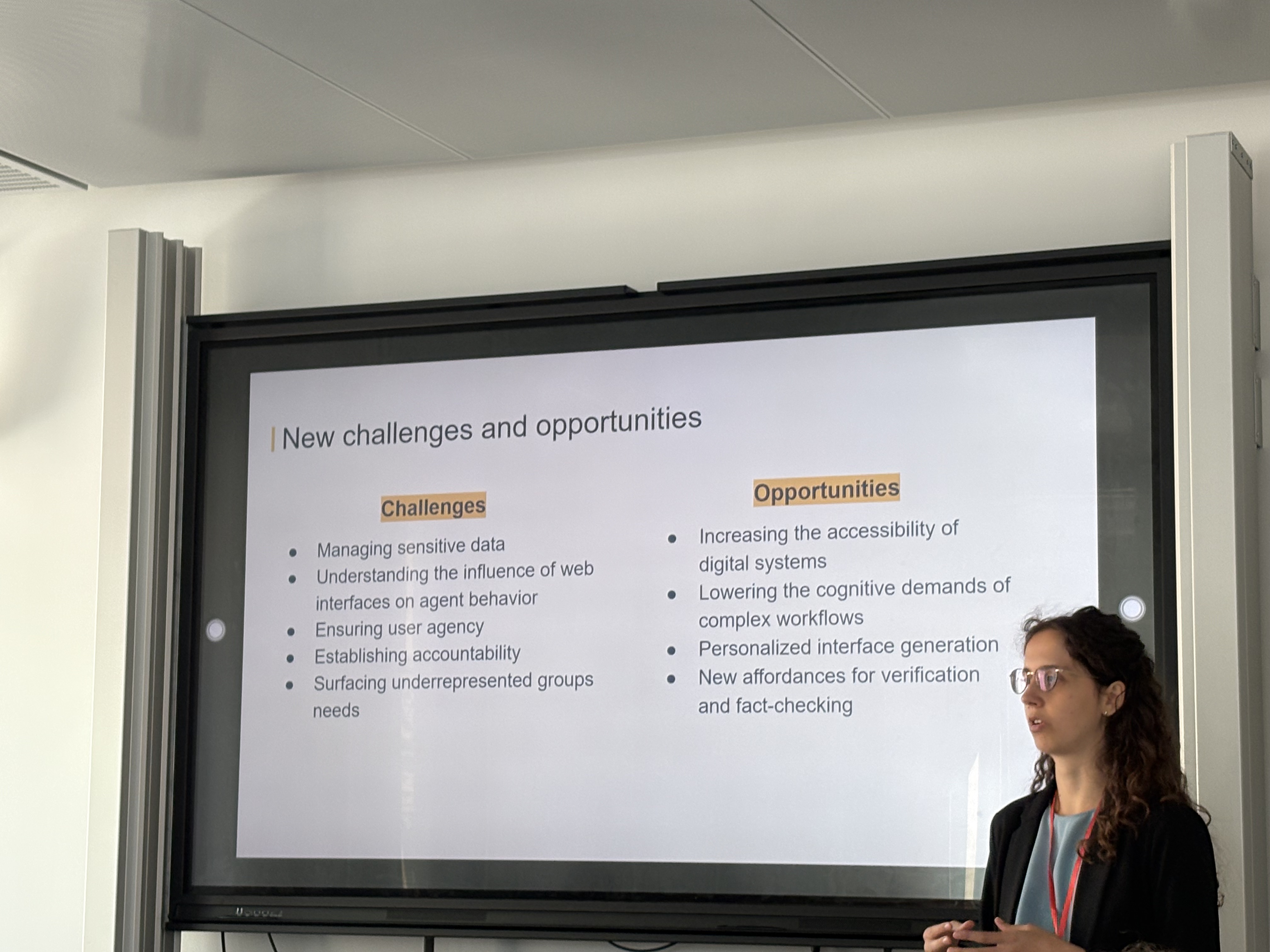 Opening presentation. The presenting organizer stands to the right of the board showing a slide with a list of challenges and opportunities that characterize conversational agentic web browsing.