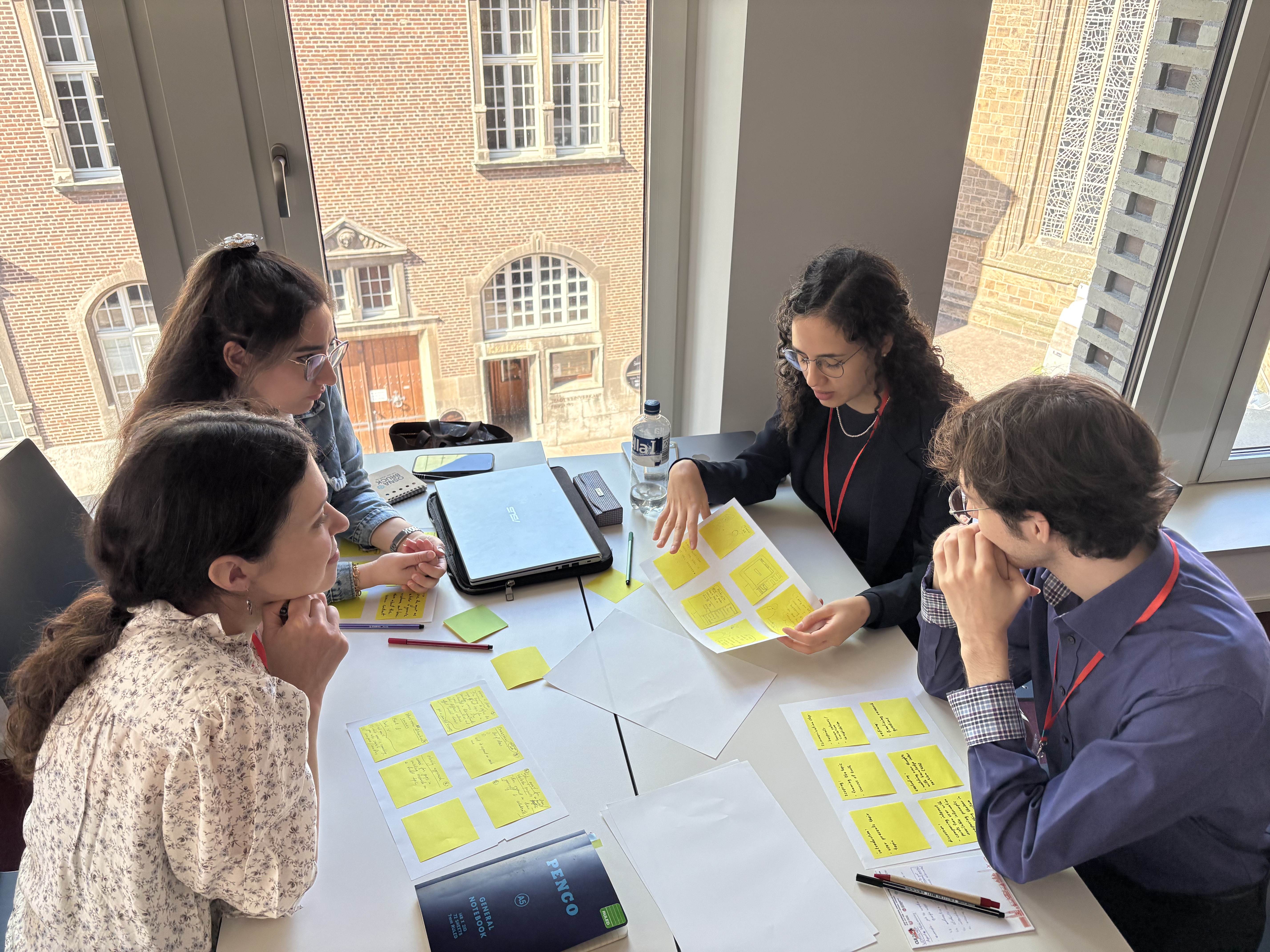 Group 1 group picture showing the four members discussing around a table one member's storyboard 