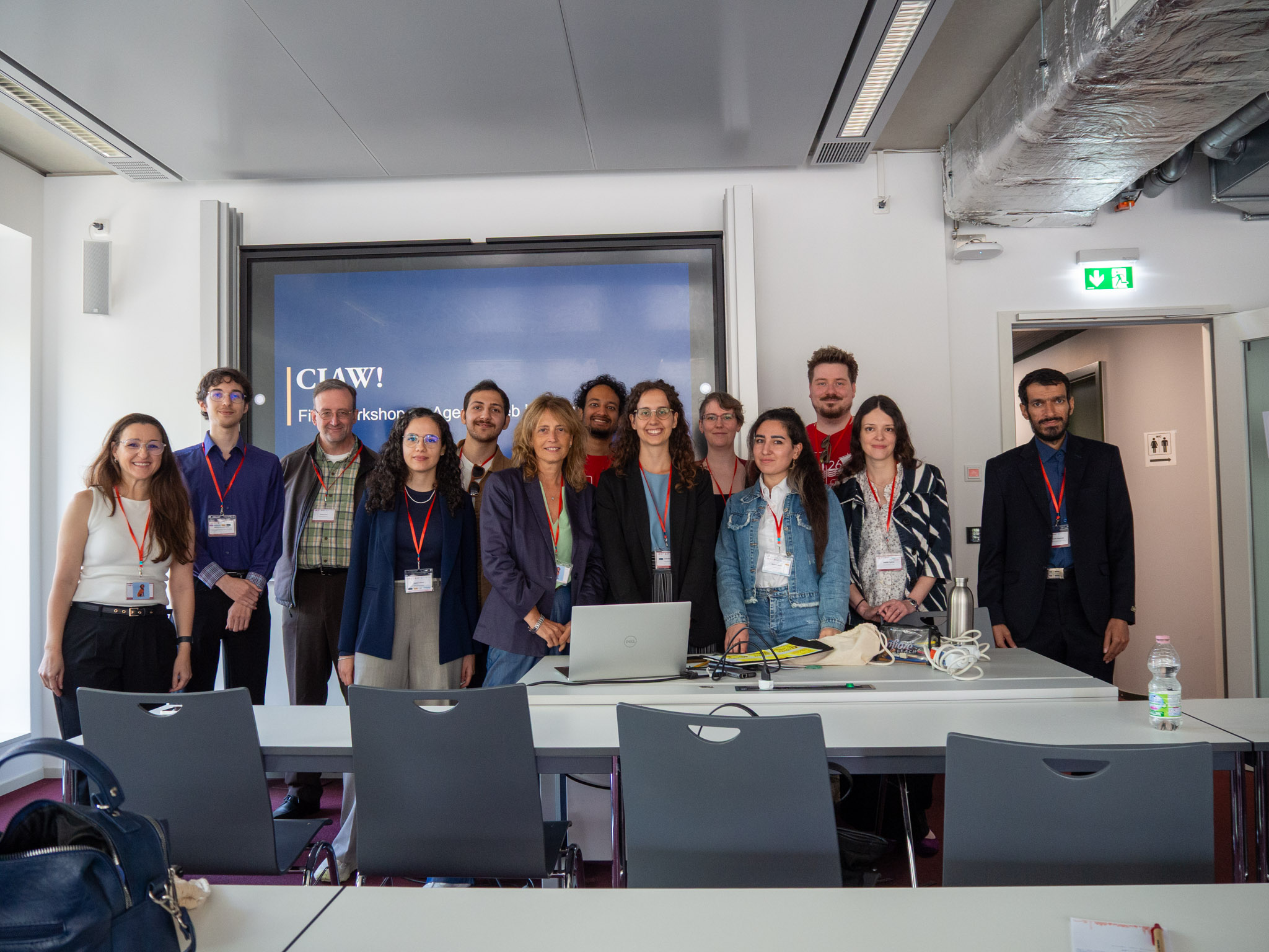 Workshop participants and organizers gathered together in front of the presentation's opening slide. Thirteen people, men and women stand together, smiling.